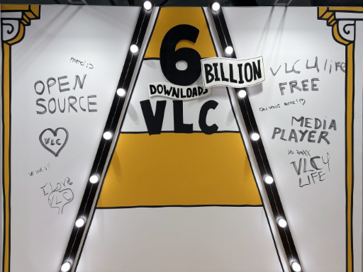 A closeup of the traffic cone that was the backdrop of the VLC CES booth. It is a big stilised orange traffic cone, with black thick lines on the sides that have lights on them. Several scribbles are on the white blank area next to the cone.