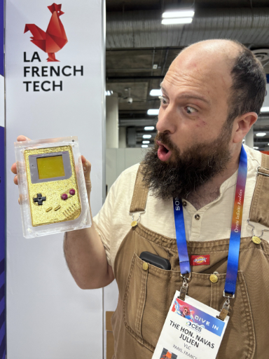 A photo of Julien looking excited at a golden, very reflective Nintendo GameBoy that he is holding up in his right hand.